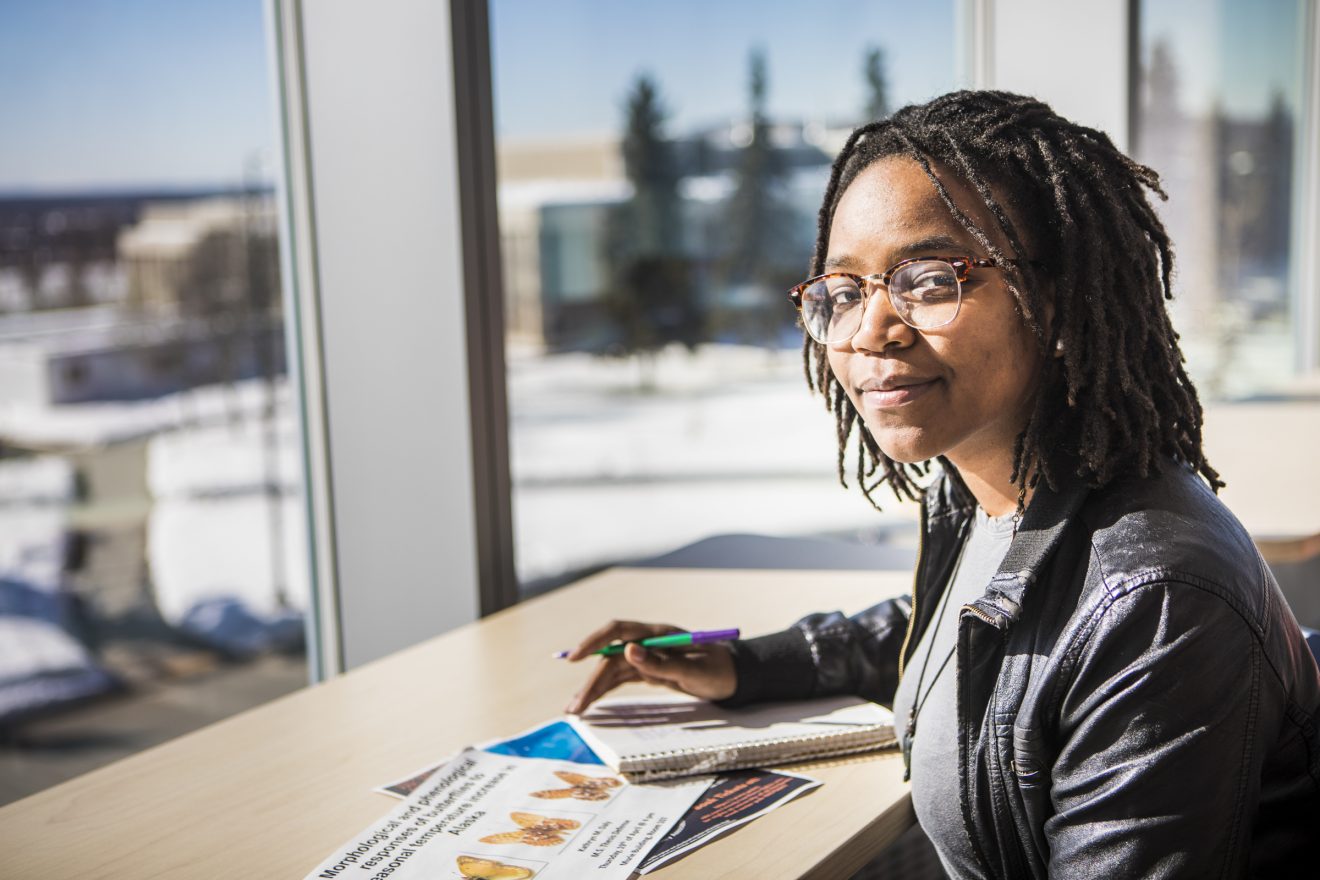 Student sitting at a table with papers and a notebook spread before her.