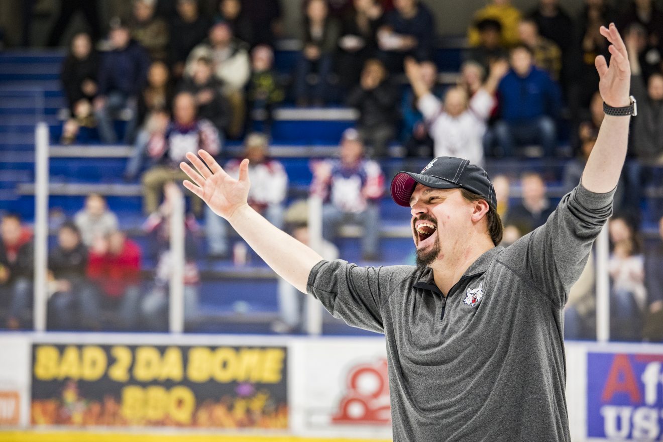 Tommy Nelson on an ice rink with his arms over his head wearing a big smile.
