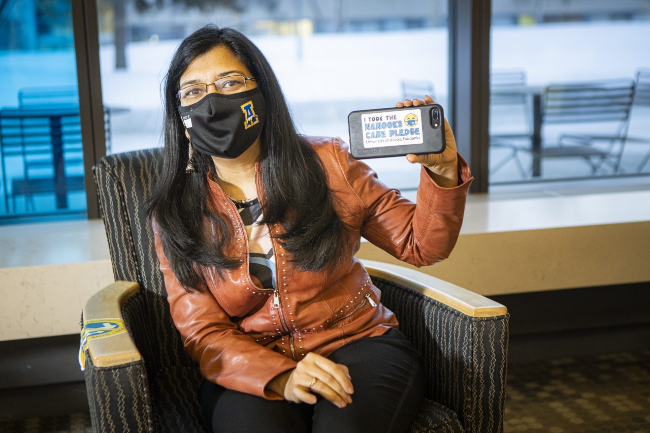 Masked woman sitting and holding a small sign saying she took the Nanooks Care pledge.