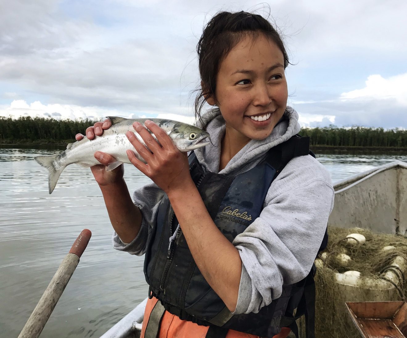 Young woman holding a fish while she sits in a boat.