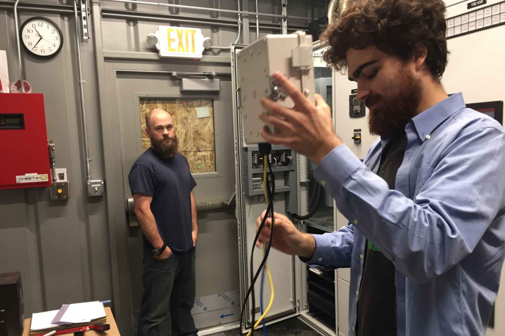 Two men stand in a mechanical room.