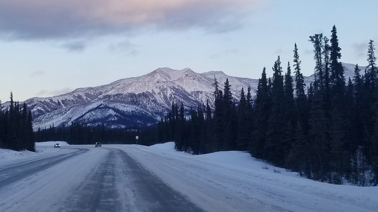 Two cars in the distance on a winter road near the mountains.