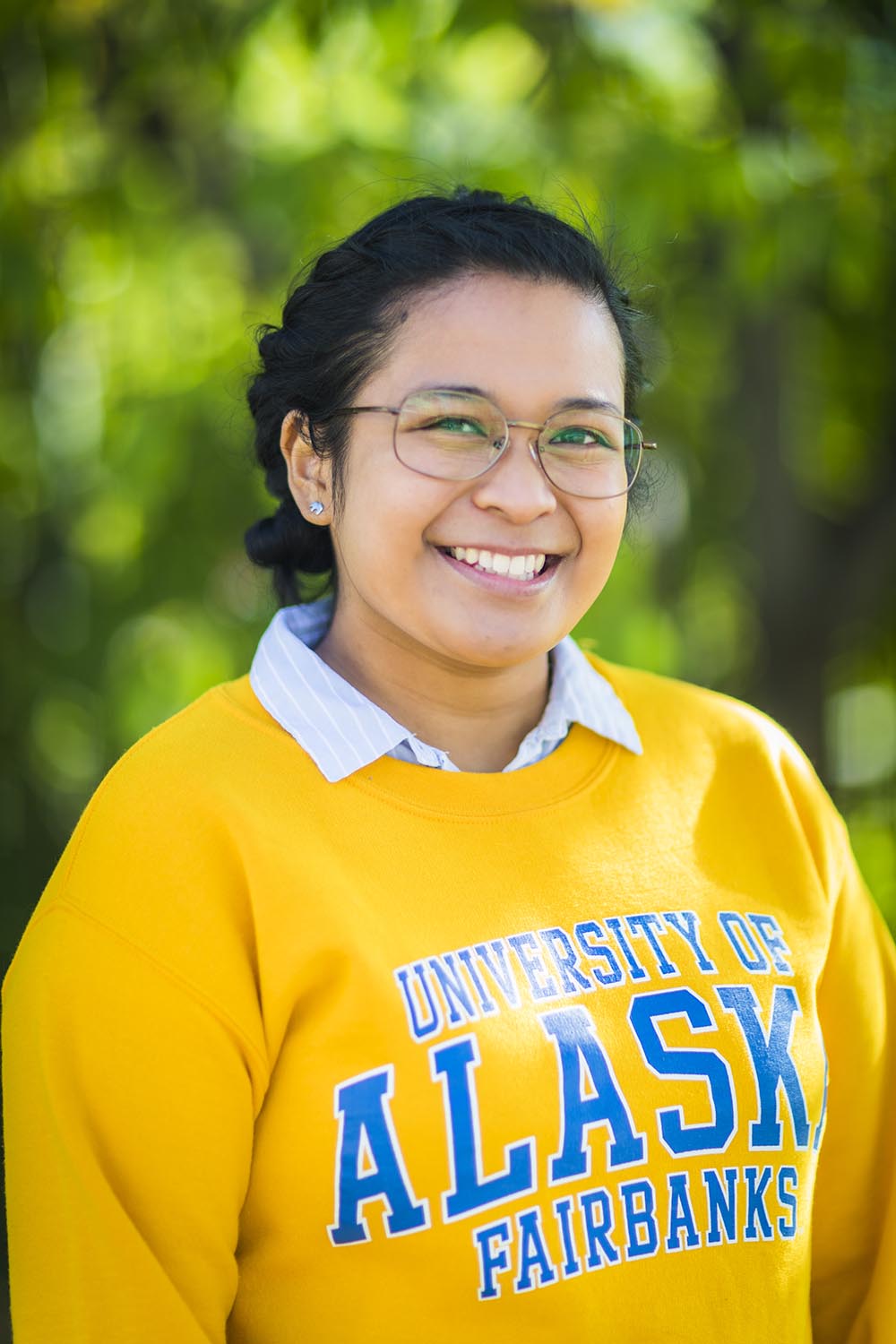 Head shot of Ray Alda. She is wearing a yellow UAF sweatshirt and is photographed outside near trees.
