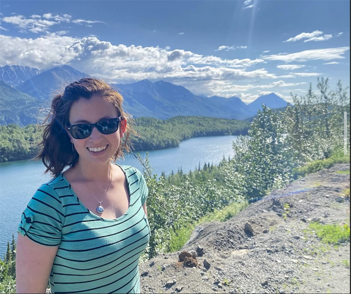 A woman smiles from a scenic view overlooking a river on a bright, clear day. photo courtesy of Jamie Simpher.