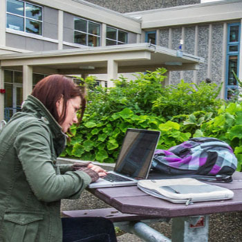 Student on a laptop outside the Arctic Health building on the Fairbanks campus