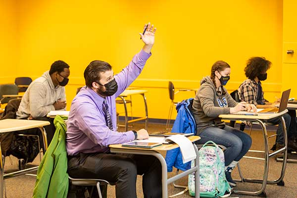 A UAF College of Business and Security Management student raises their hand during a class.