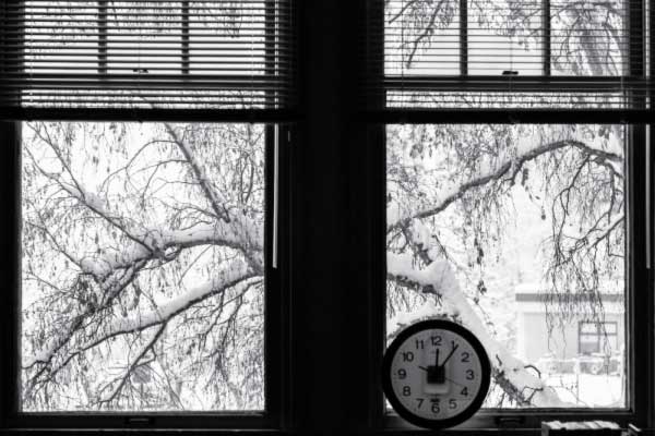A clock on a campus window ledge with snowy tree branches outside the window