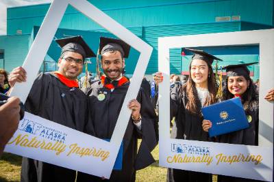 Graduates pose behind prop oversize Polaroid picture frames outside UAF commencement ceremony