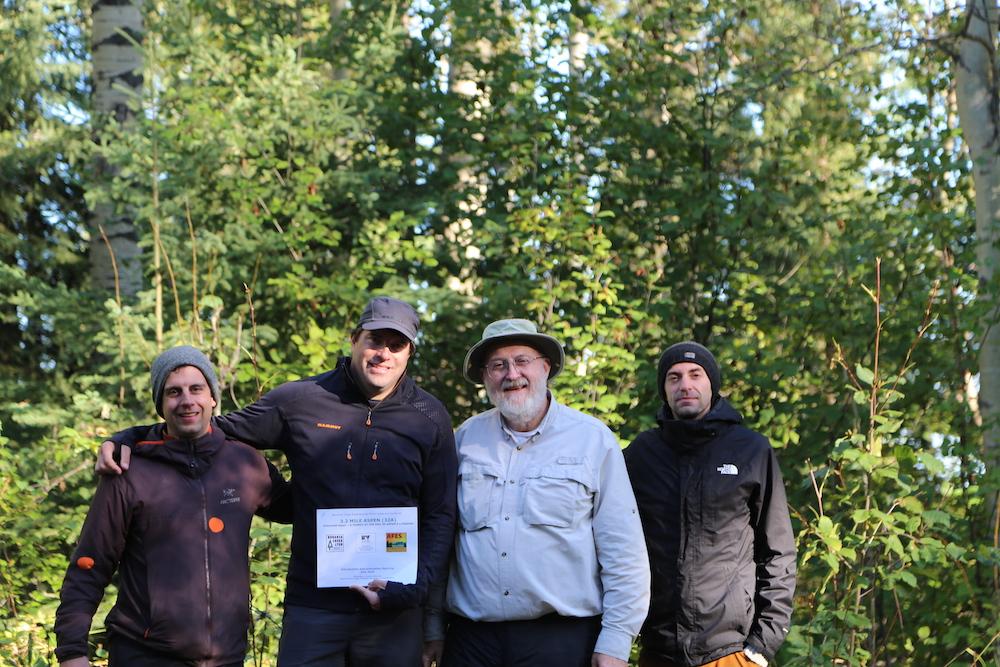 Four men stand in a wooded area