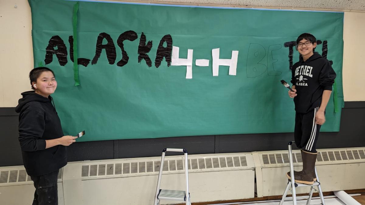 Two people painting Alaska 4-H on wall