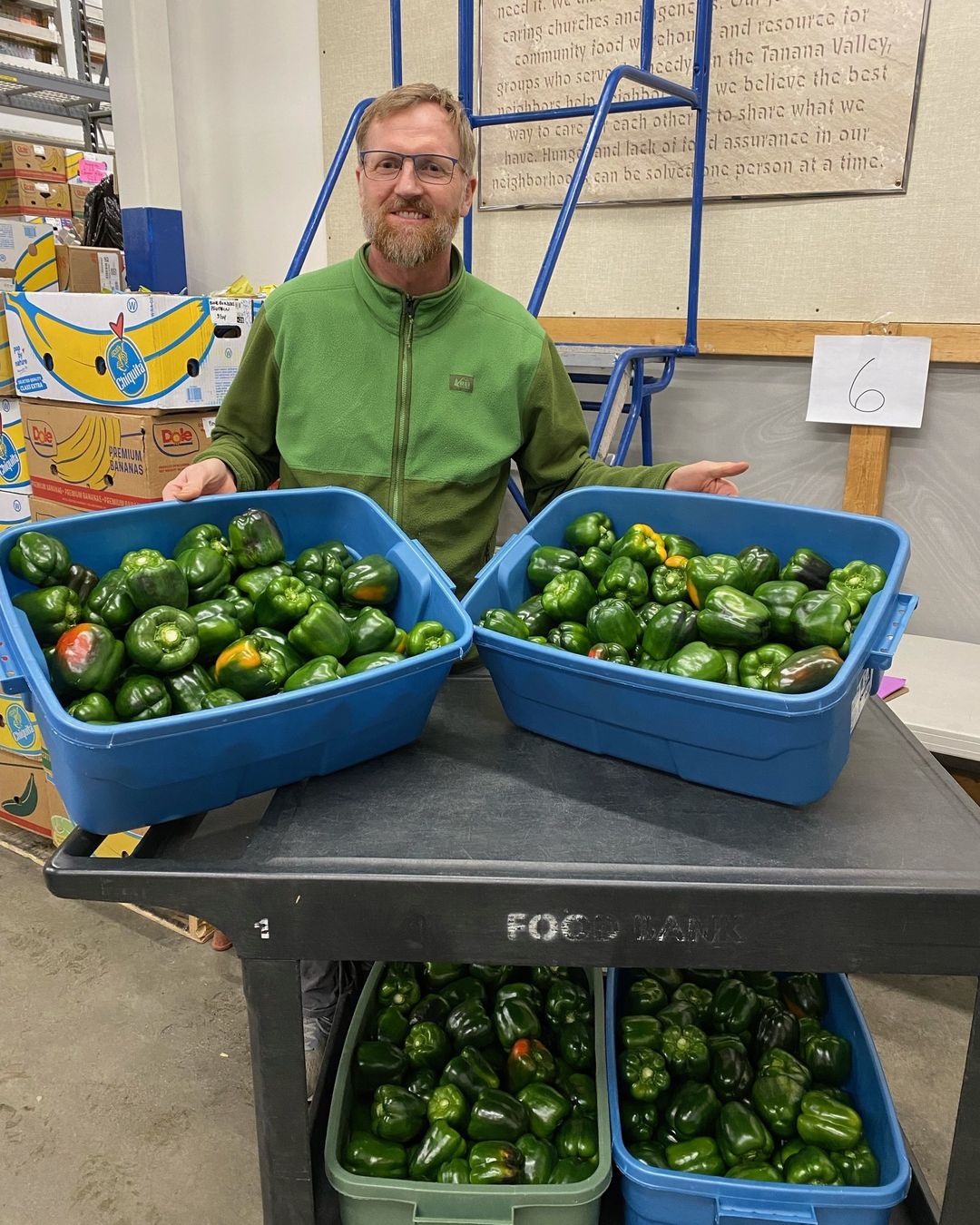 Man standing beside bins of green bell peppers