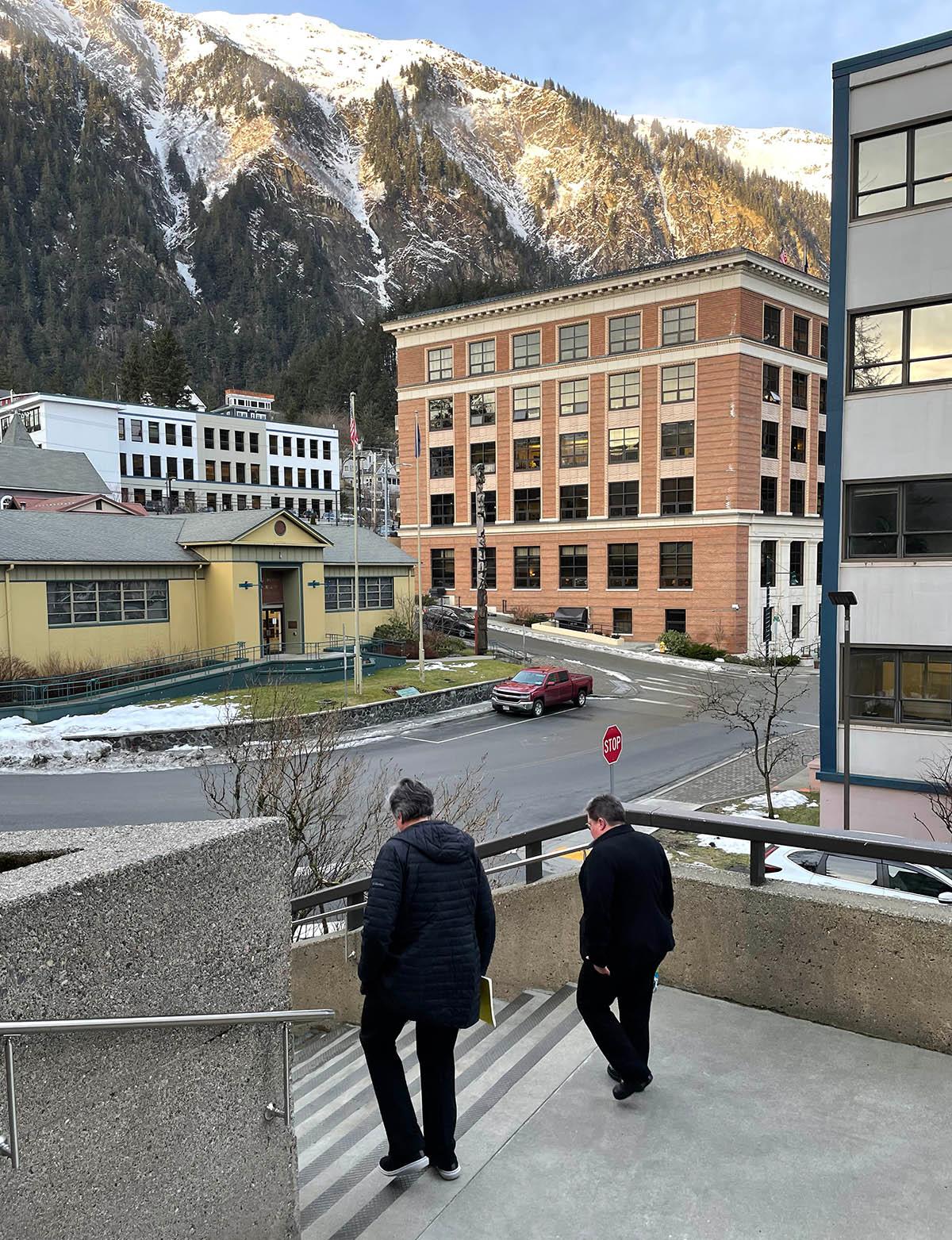 Two people stand with building and mountain in foreground