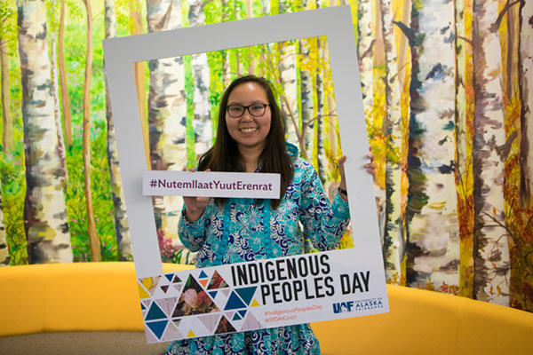 A student poses holding an oversize Indigenous Peoples Day portrait frame 