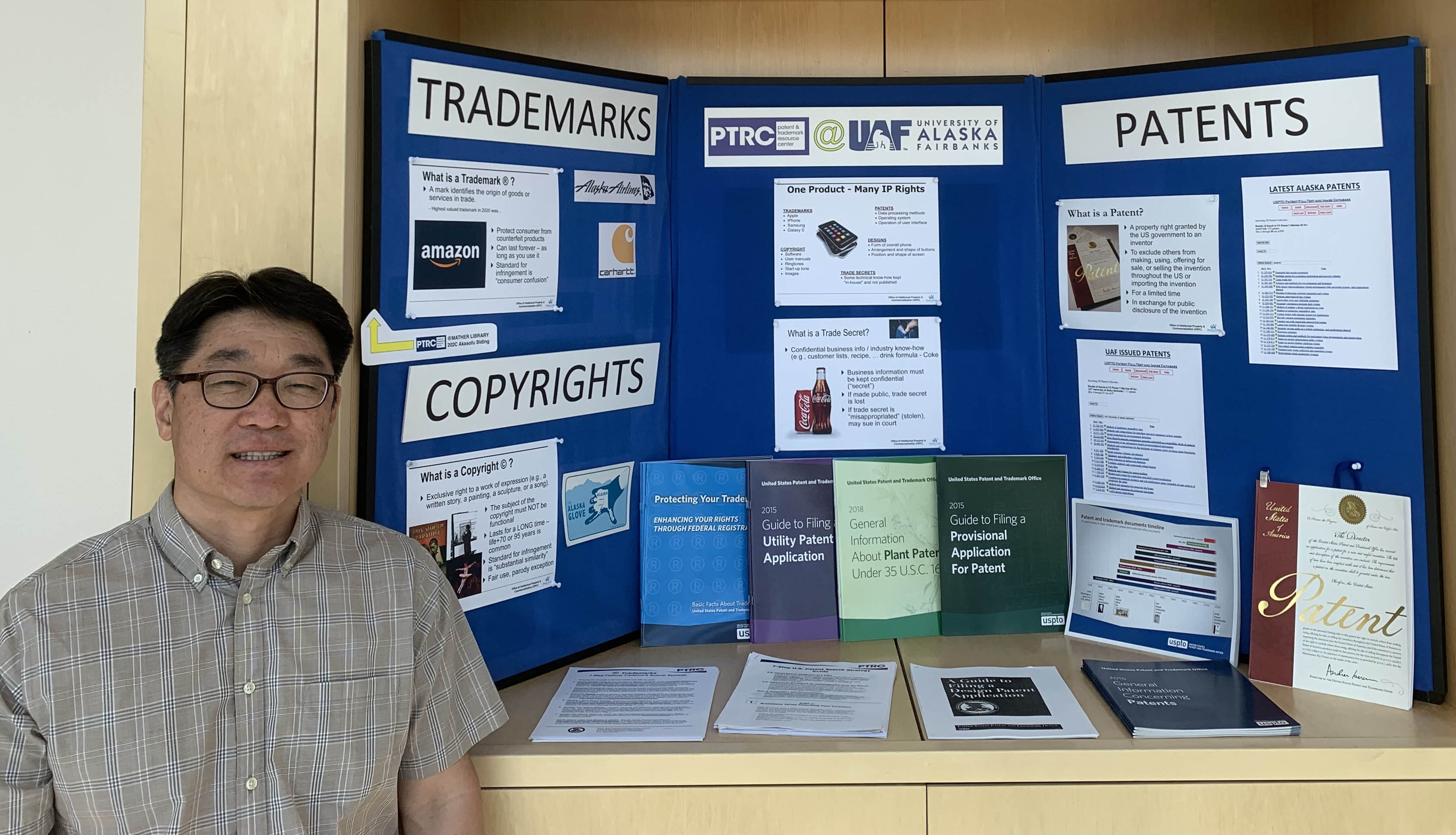 David Park poses in front of the Patent and Trademark Resource Center poster just outside of the Keith B. Mather Library on the UAF campus. Photo by Peter Park.
