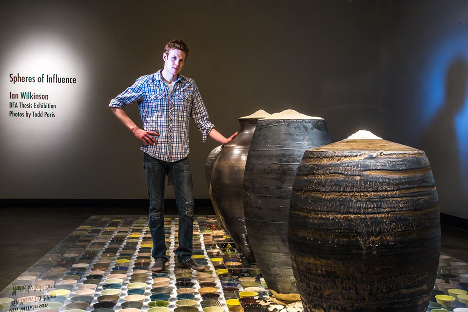 Art major Ian Wilkinson poses by one of his ceramic pieces in the UAF Fine Arts gallery. His BFA thesis project, Spheres of Influence, raised more than $18,000 for the Fairbanks Food Bank through the sale of his 1,200 bowls.