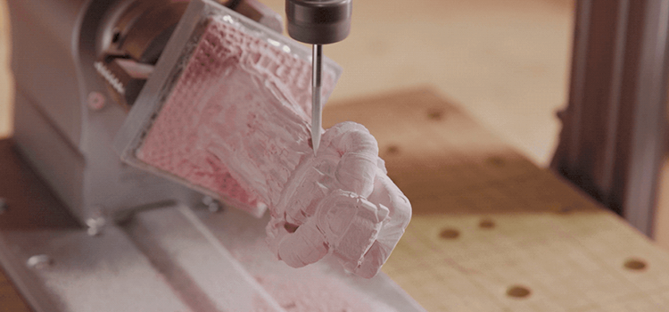 Shows a 4-axis desktop CNC machine cutting out a 3D statue