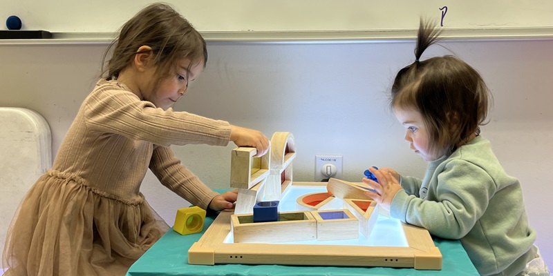Two children play with shapes on a light table