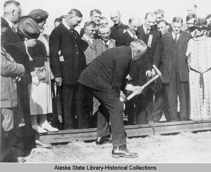 man drives a railroad spike in front of crowd