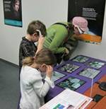 A woman and two children look at images on a table through 3-D glasses.