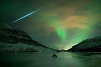 A meteor streaks across the sky, with green aurora lights in the background.