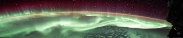 The aurora from space, hovering over the pole in red and green.