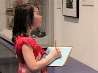 Child holding a clipboard and activity sheet, and looking at a museum exhibit.