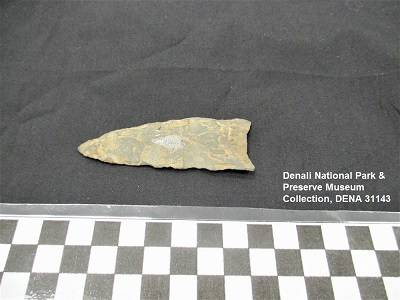 Wedge-shaped projectile point against a black background, with a centimeter ruler for scale.