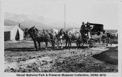 Black and white photograph of a stagecoach pulled by four horses. Wall tents are visible in the background.