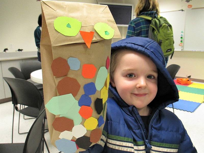 Child holding a owl puppet made from a brown paper bag and construction paper feathers.