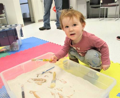 A young child digs for fossils in a sandbox.
