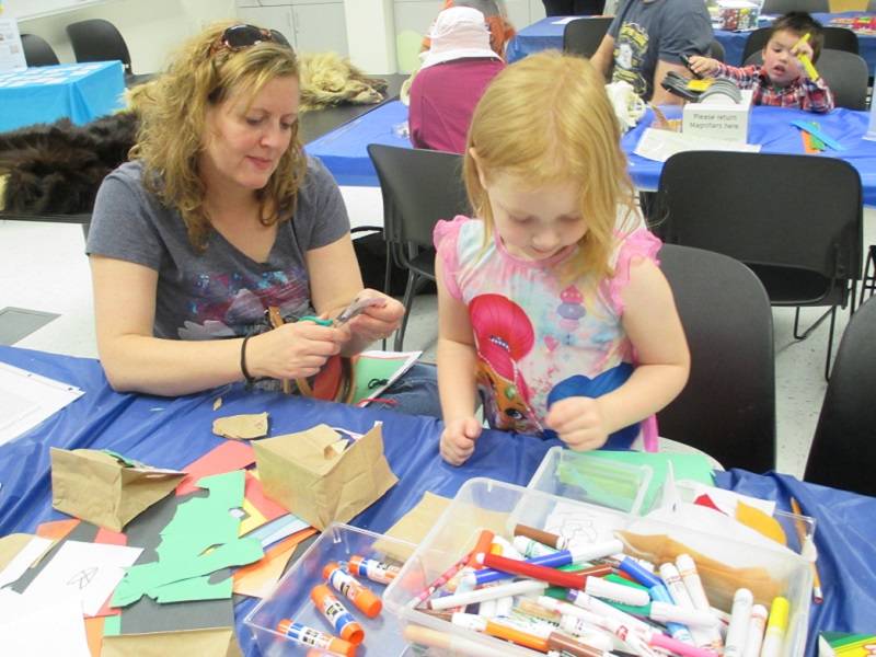 Adult and child sitting at a table with craft supplies in front of them.