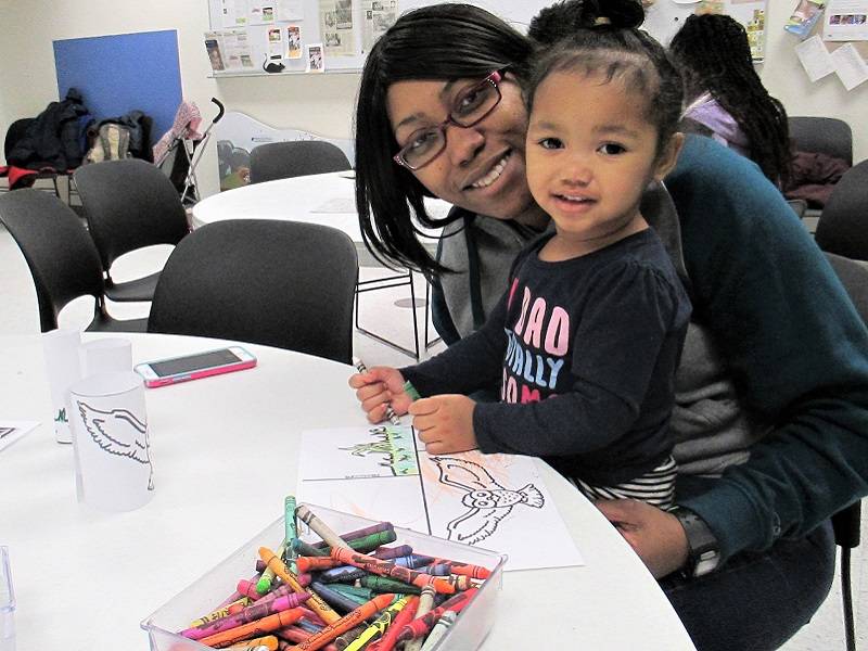 Child sitting on an adult's lap, coloring a picture of a owl.