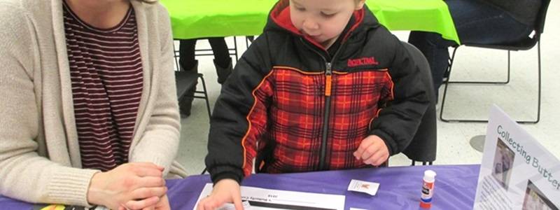 Child and adult sitting at a table gluing butterfly pictures on paper.