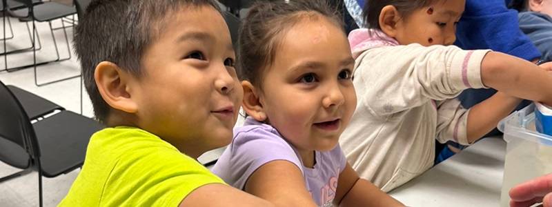 Two children smiling with their hands into Ziploc bags filled with shortening, dipping them into a tub of water.  