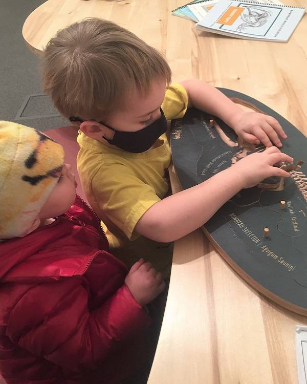 Two children put together a puzzle showing a whale skeleton.