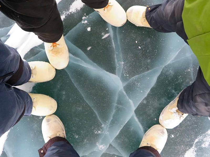 View from above of four people standing on freshwater ice. Only their feet and legs are visible.