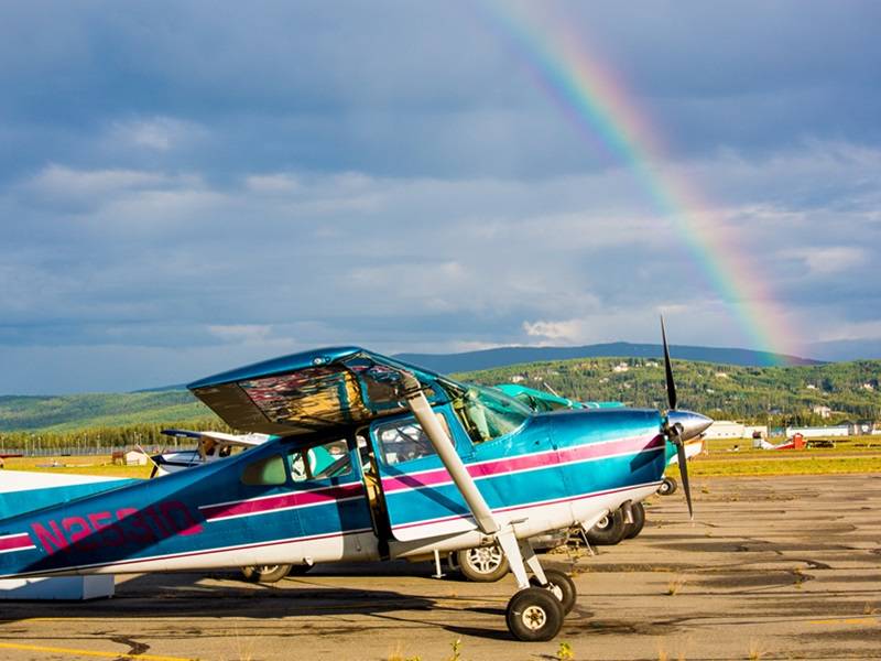 Propeller plane sitting on a runway, with a rainbow in the sky behind it.