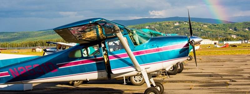 Propeller plane sitting on a runway, with a rainbow in the sky behind it.