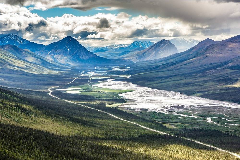 A river valley with a mountains in the background and clouds in the sky.
