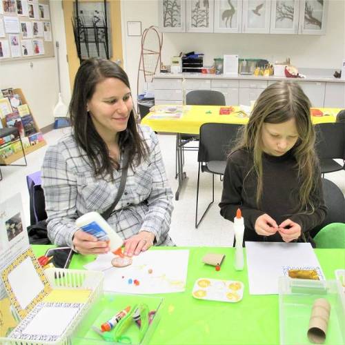 An adult and child sit at a table, making an art project.