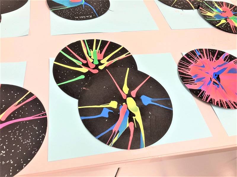 Colorful paint resembling fireworks on black circles. Several of the artworks are laid out on a counter.