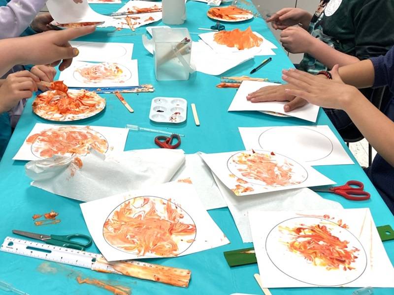 Several red-and-yellow marbled Sun prints on a table, with children's hands visible.
