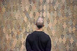 Person wearing a black sweatshirt, seen from the back, looking at a woven artwork.