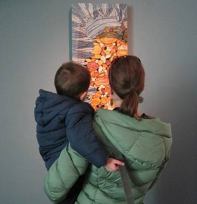 Adult holding a toddler and looking at a carving by Sara Tabbert.