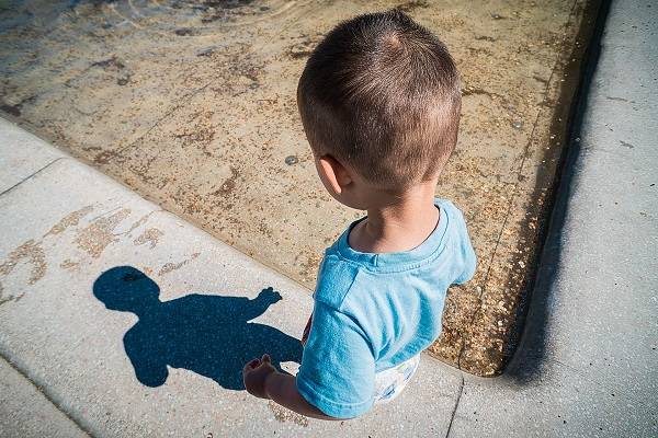A child looks at their shadow on a sidewalk.