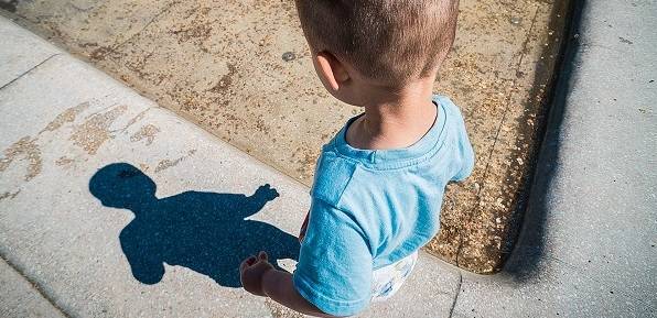 A child looks at their shadow on a sidewalk.