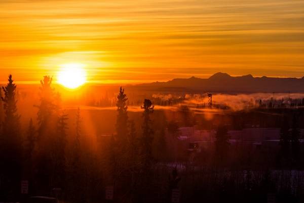 Sunrise in an orange sky, with mountains in the background and trees in the foreground.