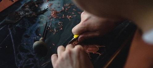 Close-up of hands carving a linocut print.