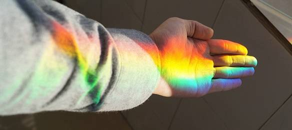 Sunlight separated into rainbow colors, shining on a child's hand.