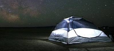 A tent set up in a field, with a starry sky in the background.